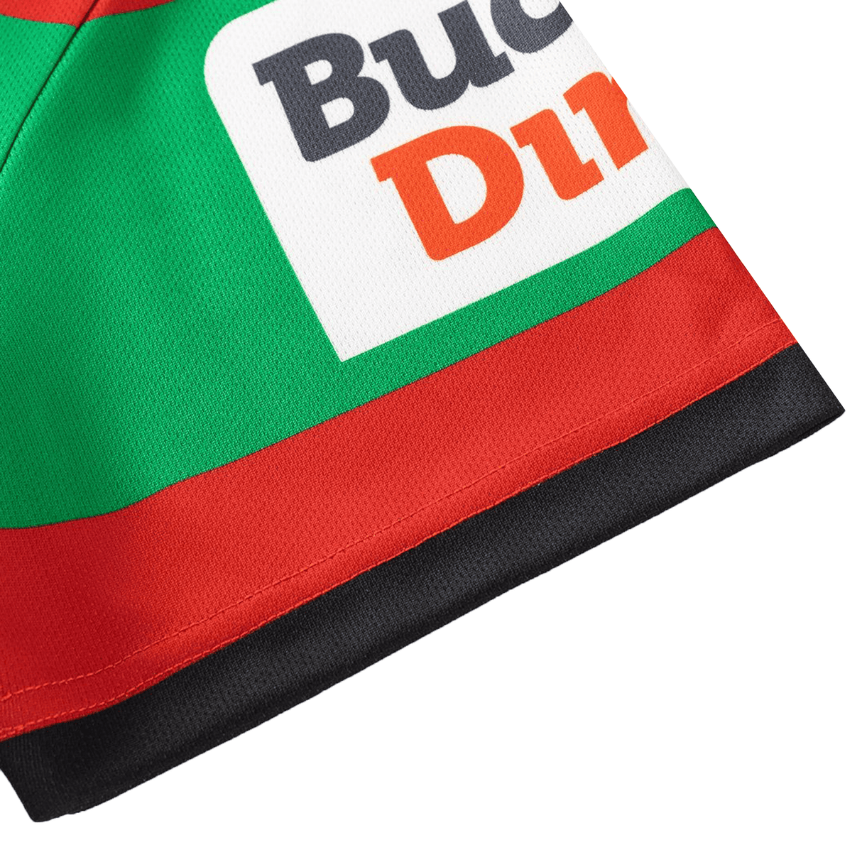 Close-up of green, red, and black fabric showing part of a printed label with "Buc" and "Din"—a detail from the Rabbitohs NRL 26/27 Replica Home Jersey by Classic Sportswear.
