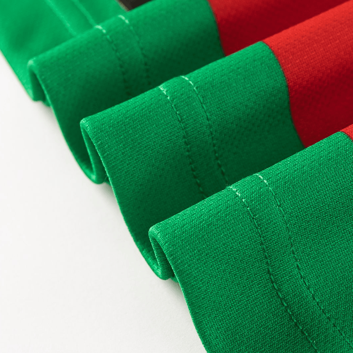 Close-up of green and red fabric with visible stitching from the Classic Sportswear Rabbitohs NRL 26/27 Replica Home Jersey, neatly folded on a white surface.