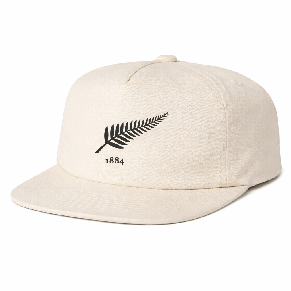 The EMB Weld Nations of Rugby New Zealand Vintage Brushed Cotton Cap is a beige snapback hat with a black fern leaf and "1884" on the front, inspired by vintage NZ rugby caps for a comfortable, adjustable fit.