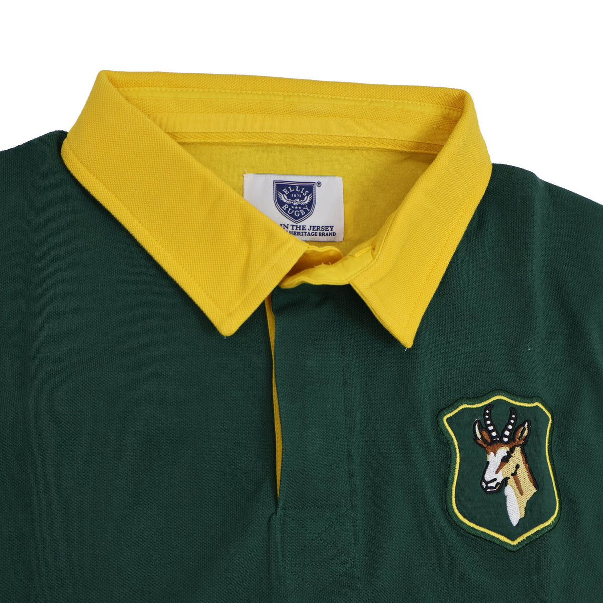 South Africa Rugby Polo 1924 by Ellis Rugby features a green design with a yellow collar and an embroidered antelope badge on the chest, inspired by the classic Springbok rugby style. A white clothing label is visible inside the collar, reflecting the heritage of Ellis Rugby and celebrating South Africa’s rugby polo tradition.