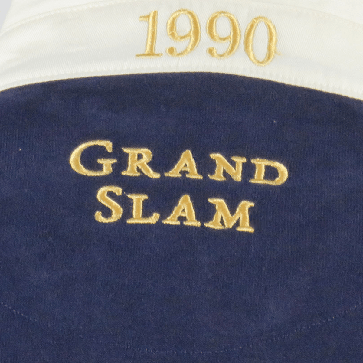 Close-up of the Ellis Rugby Scotland 1990 Grand Slam Classic Rugby Shirt, featuring "Grand Slam" embroidered in yellow and "1990" in gold on dark fabric, celebrating Scotland's iconic 1990 victory, set against a white background.