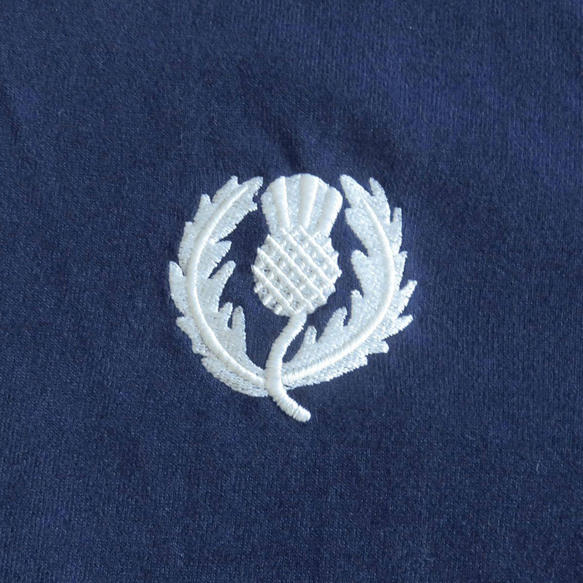 The Scotland 1990 Grand Slam Classic Rugby Shirt by Ellis Rugby boasts a white thistle emblem on dark blue fabric, capturing a historic moment with timeless elegance.
