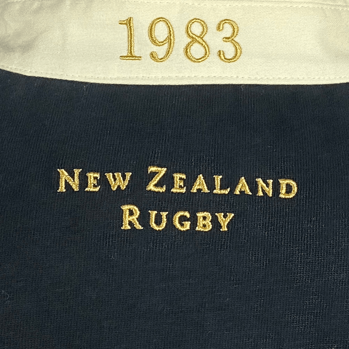Close-up of the Ellis Rugby All Blacks 1983 Classic Rugby Shirt, featuring "1983" on the collar with "New Zealand Rugby" beautifully embroidered in gold on black fabric, reminiscent of an All Blacks shirt.