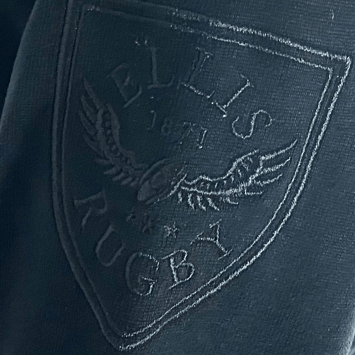 Close-up of the Ellis Rugby logo on the All Blacks 1983 Classic Rugby Shirt, featuring a vintage-style rugby ball and eagle crest with the year 1871.