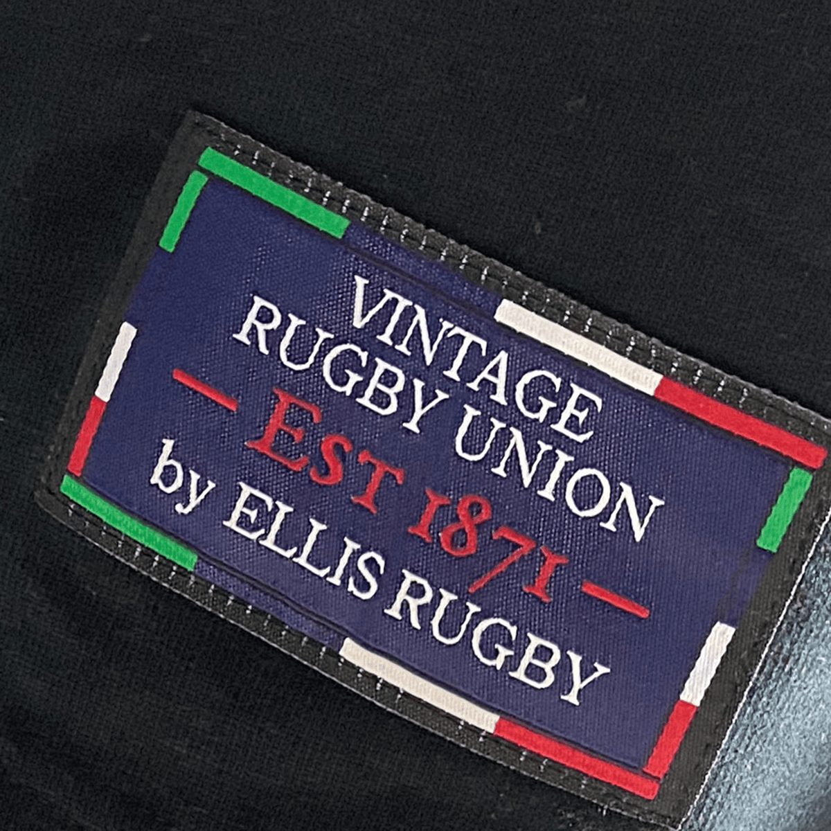 Label displaying "Ellis Rugby All Blacks 1983 Classic Rugby Shirt" on a blue background with colored border, capturing the classic charm of a Cotton Rugby Top.