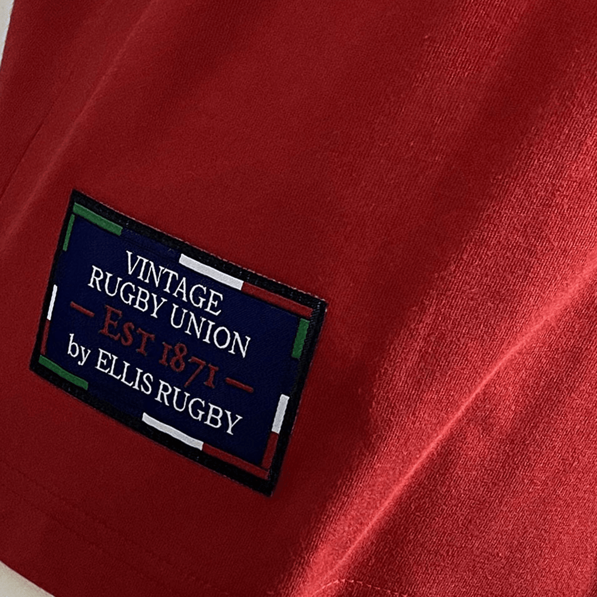 A close-up of the Ellis Rugby Canada Rugby 1932 T-Shirt in vibrant red showcases a rectangular patch reading "Vintage Rugby Union Est 1871 by Ellis Rugby," bordered with elegant red, green, and white stripes, capturing the spirit of Canada Rugby 1932.