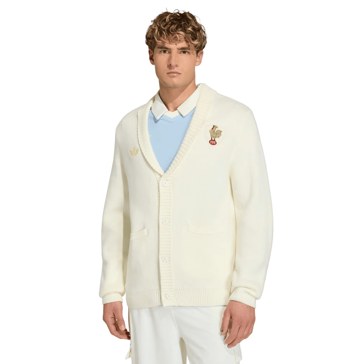 A young man models the France FFR 120 Year Cardigan by adidas, featuring a chest patch, over a pale blue shirt and white pants, against a plain white background—showcasing classic French rugby heritage.