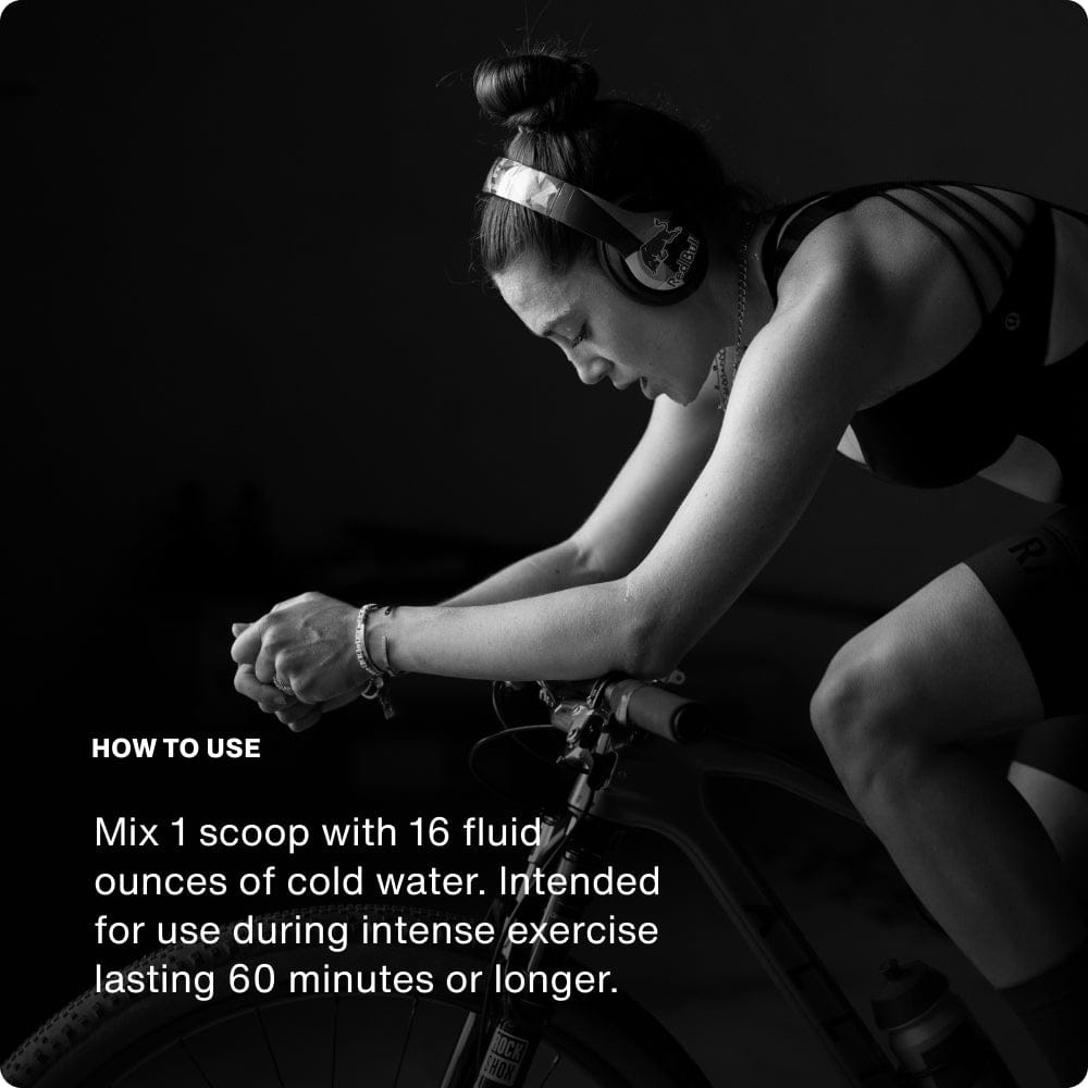 A woman in athletic wear rides a stationary bike indoors, wearing headphones. In the lower left, instructions explain how to mix Momentous Fuel by Momentous for sustained energy during intense exercise.