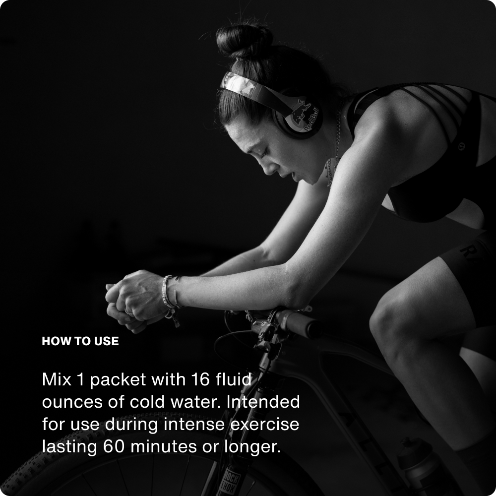 A person wearing headphones rides a stationary bike indoors. Text shares mixing instructions for Momentous Fuel 10-Travel Packs by Momentous, a carb electrolyte formula made to sustain energy and boost endurance during intense workouts over 60 minutes.