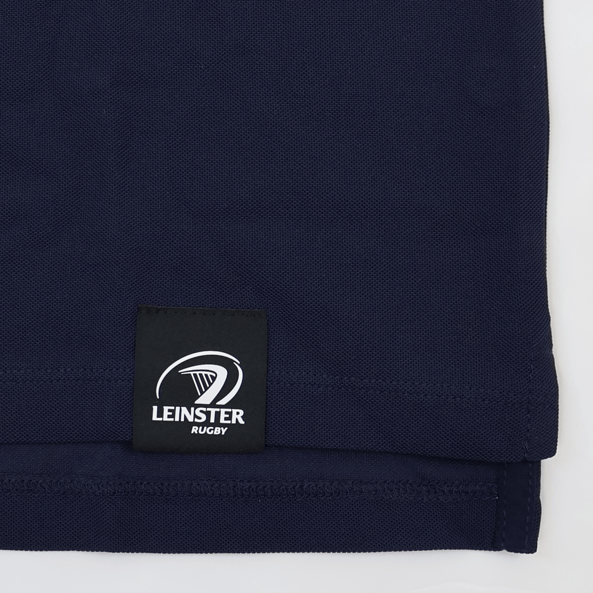 A close-up of the hem of the Leinster 24/25 Club Essential Polo by Castore, featuring a sewn-on label with the Leinster Rugby logo and text.