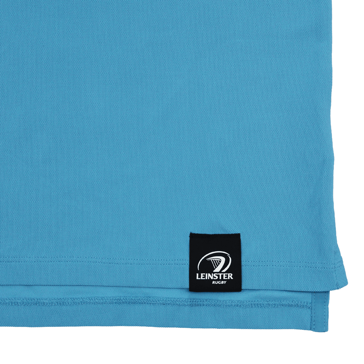 Close-up of the lower hem of the Castore Leinster 24/25 Club Essential Polo in light blue, showing a black label with the Leinster Rugby logo in white.