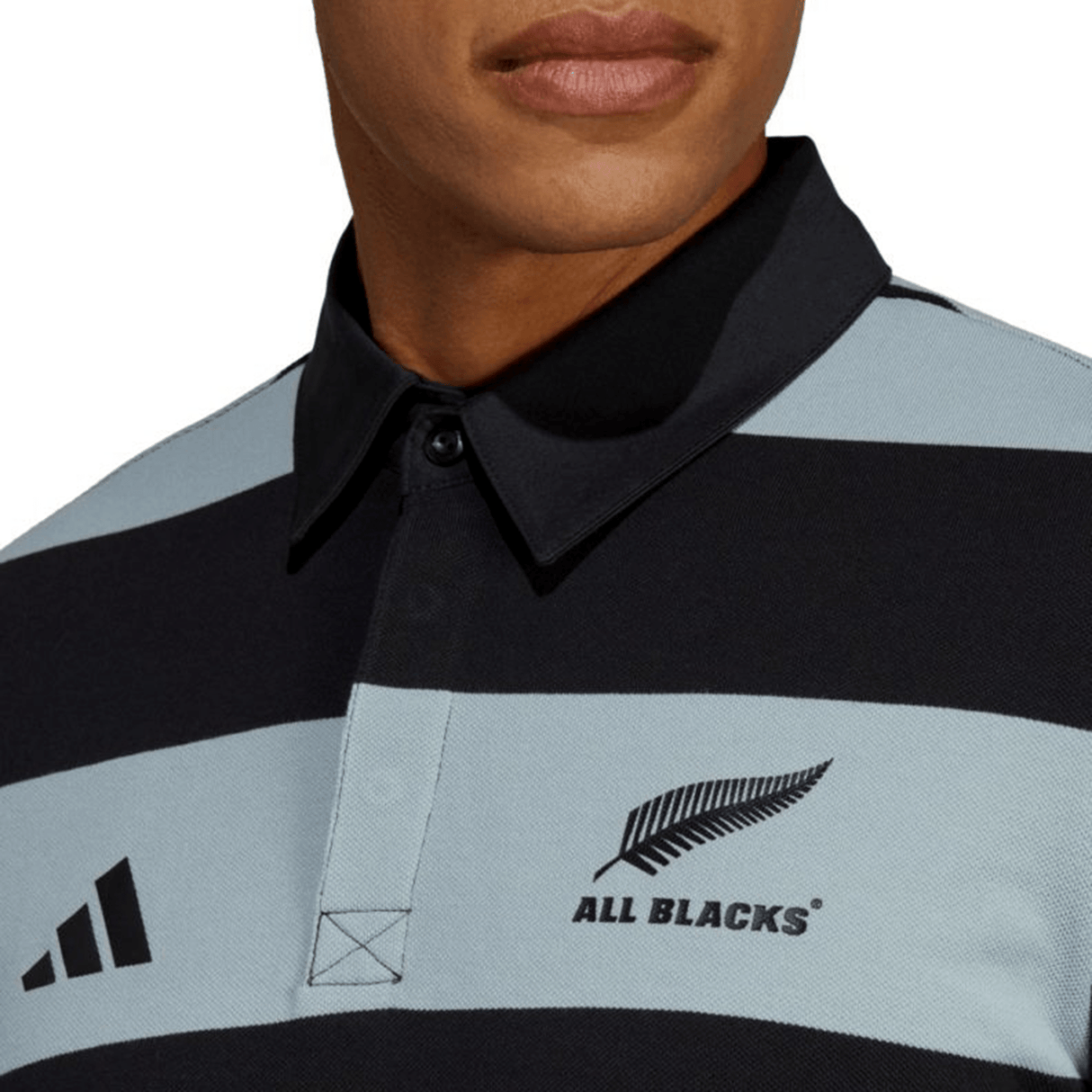 Close-up of a person wearing the All Blacks Supporters Polo by adidas, featuring black and light blue horizontal stripes, the All Blacks team badge, and an adidas logo. The person's face is partly visible.