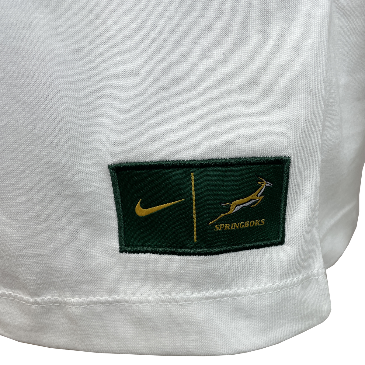 Close-up of the Nike Springboks 25 Bokke Just Do It T-Shirt: white fabric with a green patch featuring the Nike logo and "SPRINGBOKS" emblem, capturing the iconic Just Do It spirit.