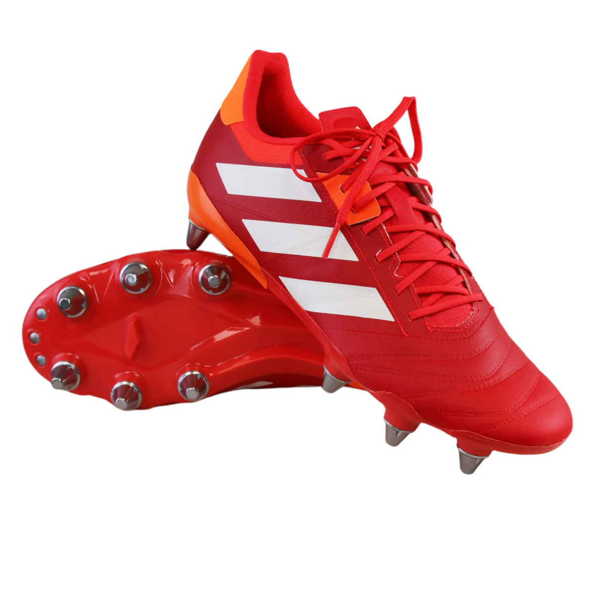 The adidas Kakari RS SG soccer cleats in Lucid Red/White/Team Solar Orange feature white stripes and eight metal studs, with one upright and the other sole-up, displayed on a white background.