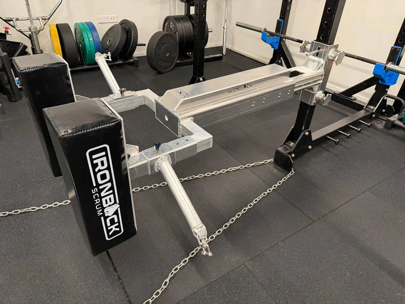 An IronBack Iron Back Force Trainer is positioned on a gym floor, surrounded by weights and fitness equipment—perfect for developing isometric strength and the horizontal pushing power essential for rugby performance.