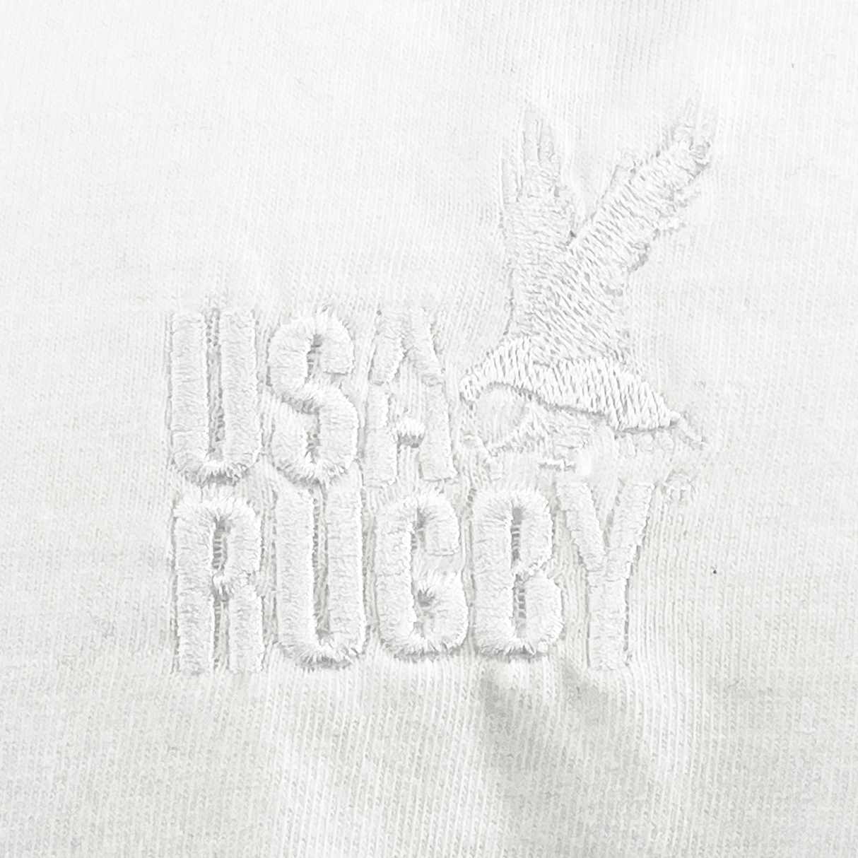 The EMB S&S Activewear USA Rugby Elevated Throwback Tonal Comfort Tee features white embroidered "USA Rugby" text and an eagle logo on white fabric, offering fans a timeless, classic look in a comfortable throwback style.