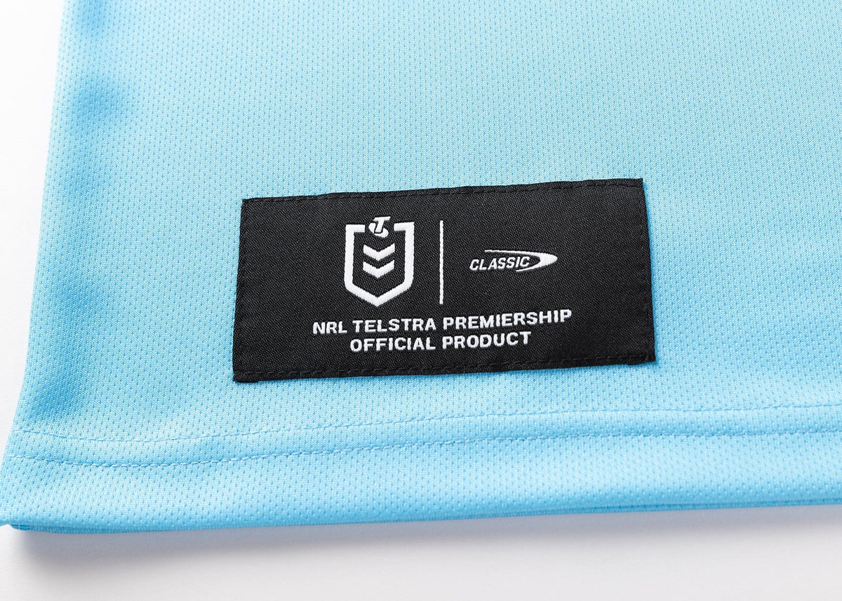 A light blue fabric similar to the Sharks NRL 25/26 Replica Home Jersey by Classic Sportswear, featuring a black patch with the NRL Telstra Premiership logo and "Classic".