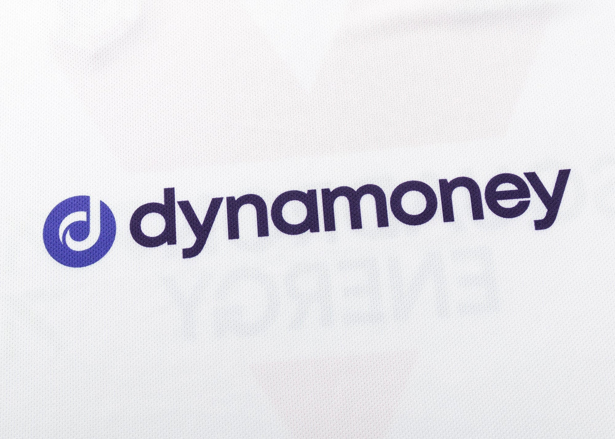 The image displays "dynamoney" in blue lowercase on white, with a blue circular logo to the left, resembling the distinct style of Classic Sportswear's Dragons NRL 25/26 Replica Home Jersey.