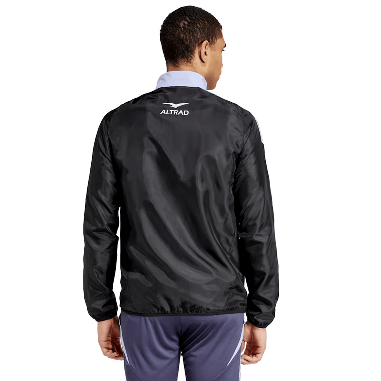 A person wearing an adidas All Blacks 24/25 Presentation Jacket featuring "Altrad" on the back is facing away, looking slightly to the side. They sport dark pants and a light shirt underneath, with a subtle silver fern pattern visible.