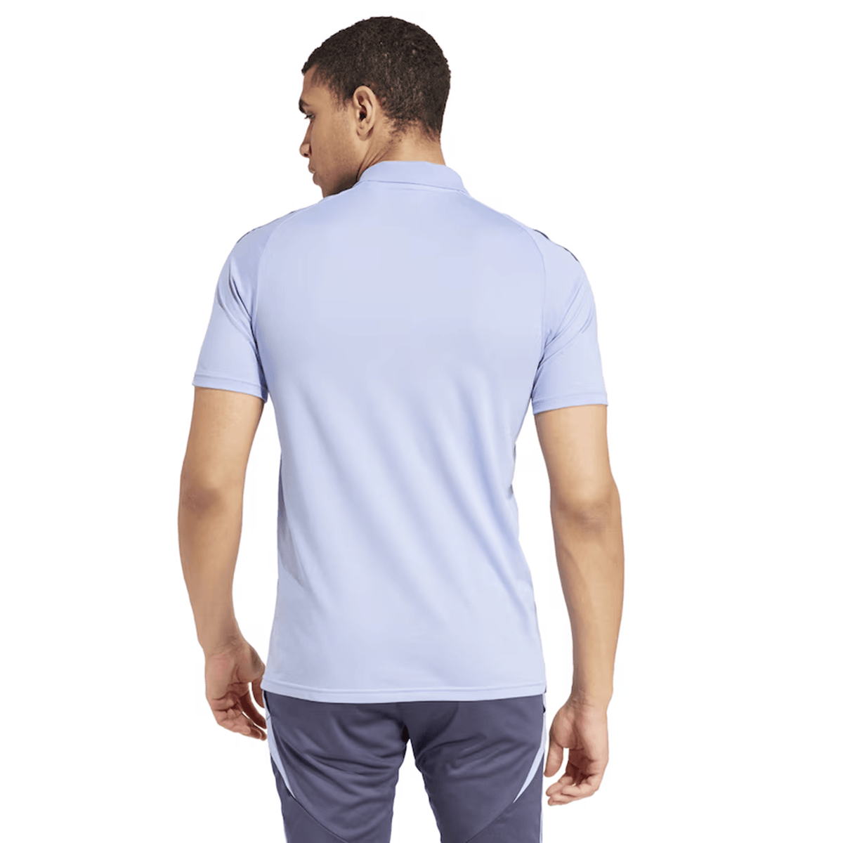 A person wearing the All Blacks 24/25 Performance Polo by adidas in light blue, paired with dark pants, stands with their back to the camera, embodying the iconic style of New Zealand's renowned rugby team.