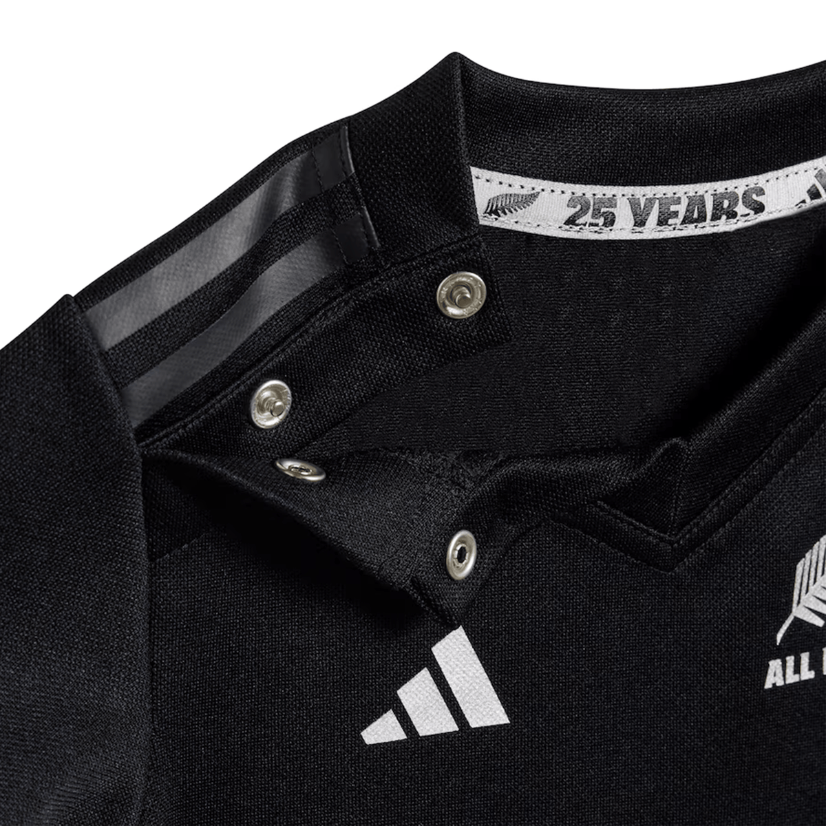 Close-up of an adidas Infant All Blacks 24/25 Home Kit sports jersey collar with snap buttons, featuring white logos and "25 YEARS" text, crafted with AEROREADY Technology.