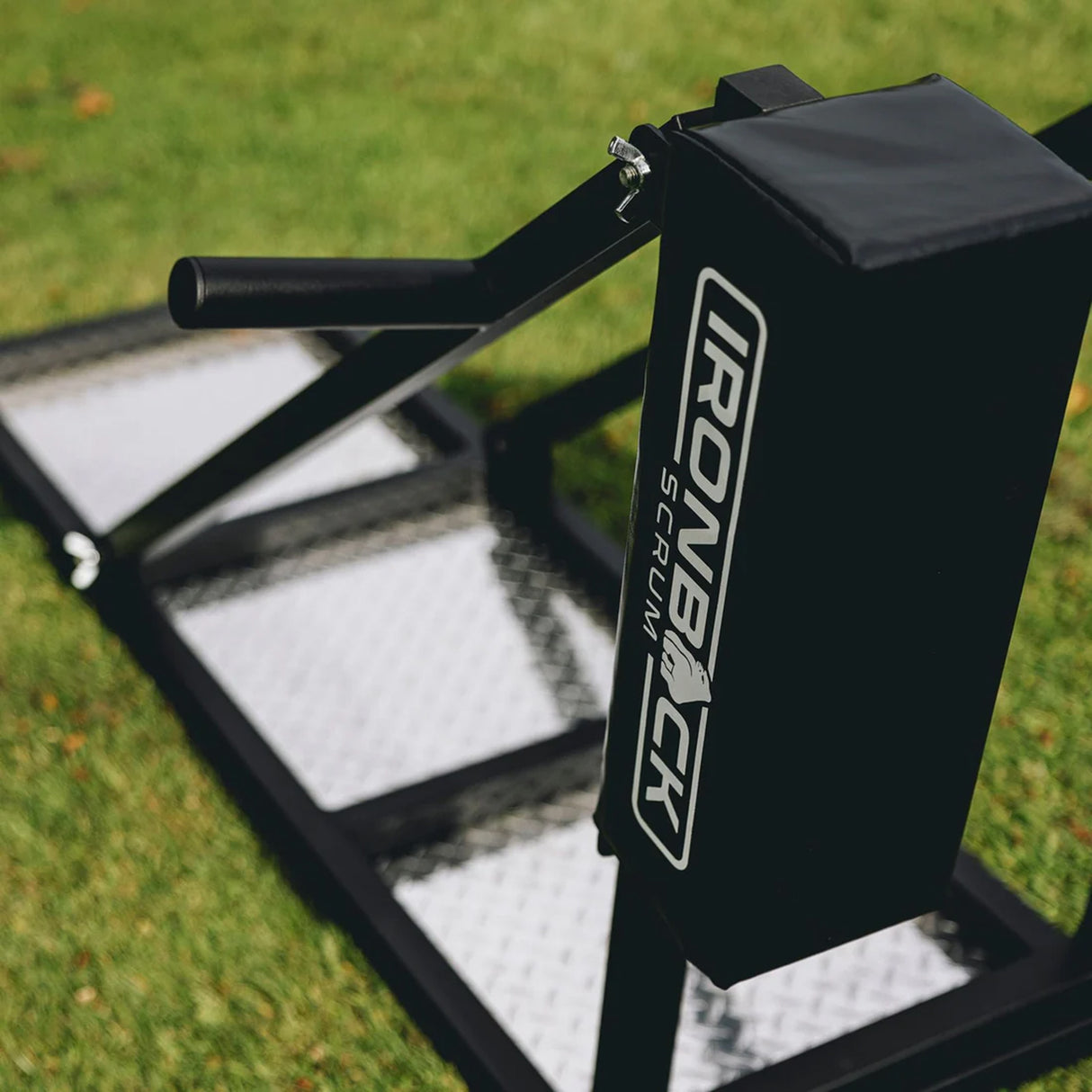 A close-up of the IronBack Iron Back Sharpener Scrum Sled, featuring padded arms and metal footplates on grass—essential rugby training equipment from IronBack, perfect for improving strength and footwork.
