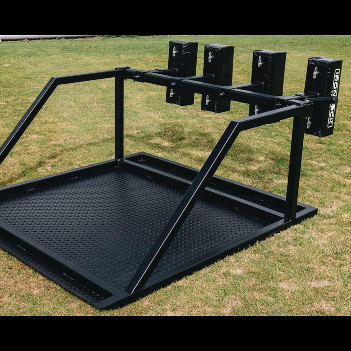 An IronBack Iron Back Gorilla 8 Man Scrum Machine, featuring a black metal frame and padded arms, is positioned on a grassy field.