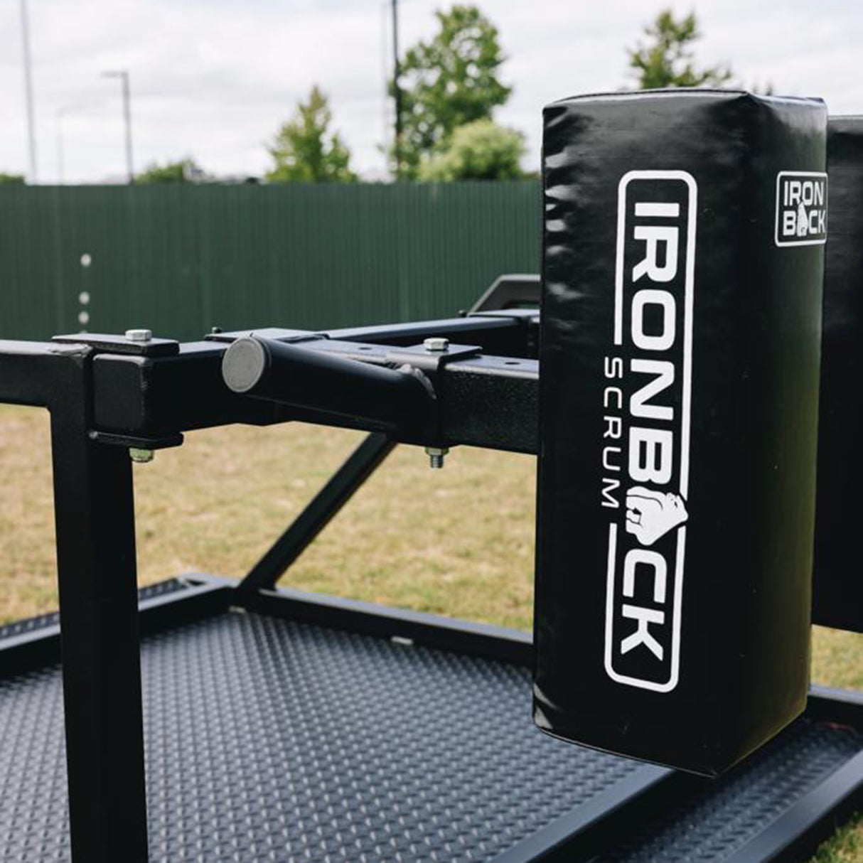 Close-up of a black IronBack Scrum training pad mounted on the Iron Back Gorilla 8 Man Scrum Machine, positioned outdoors on grass with trees and a green fence in the background—an essential piece of scrum training equipment for any professional rugby team.
