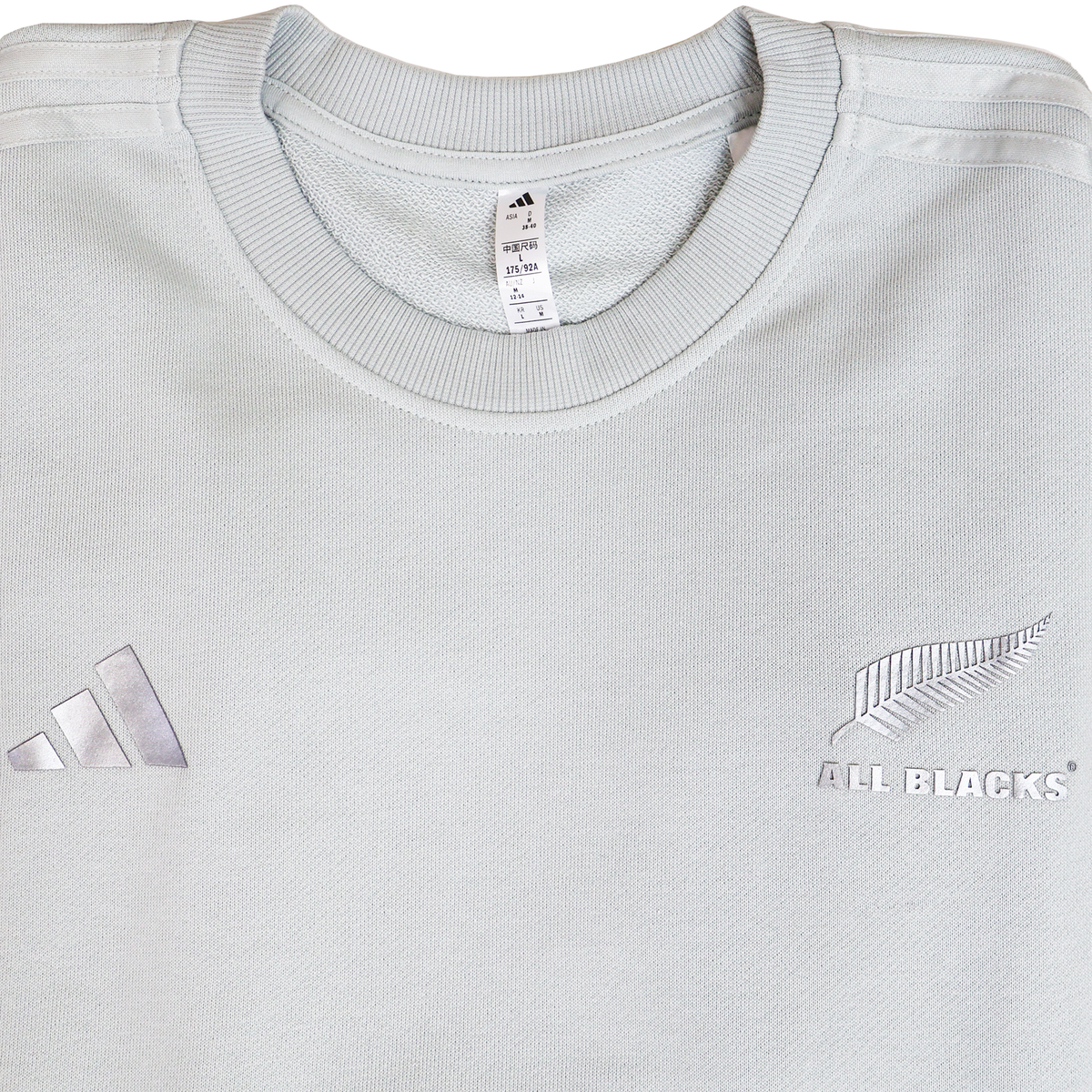 The Women’s All Blacks 24/25 Fan Crewneck Sweatshirt by adidas is a light gray top with the adidas logo on the left chest and silver fern on the right—ideal for female supporters.
