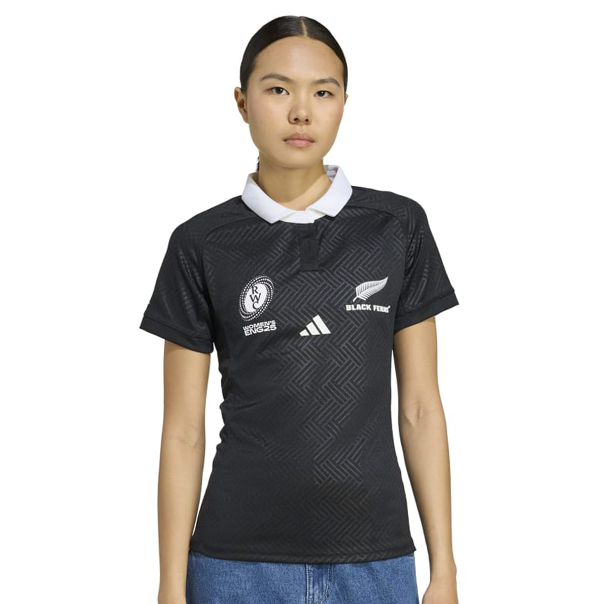 A woman wears the adidas Women's Black Ferns WRWC25 Replica Home Jersey, featuring a white collar and team logos, standing against a plain background with a neutral expression.