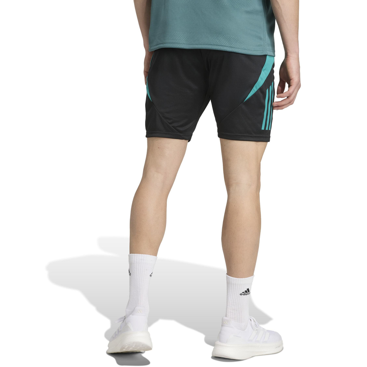 A person stands facing away, wearing adidas All Blacks 25/26 Training Gym Shorts with teal stripes, a teal shirt, white crew socks, and classic adidas sneakers.