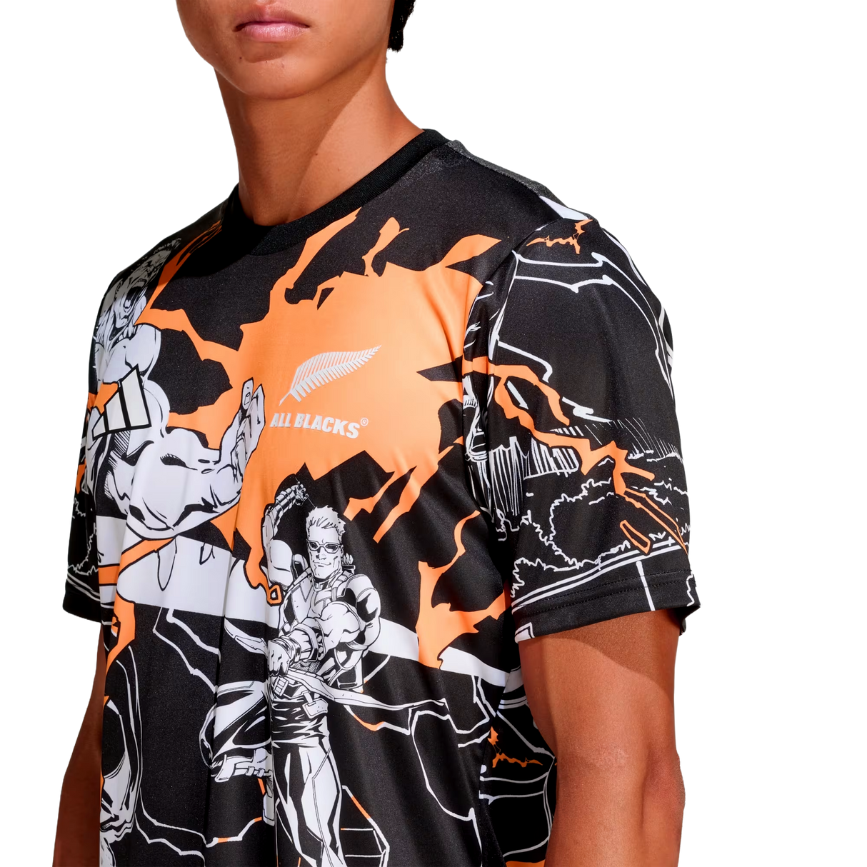 A person wears the adidas All Blacks 26/27 Captains Run Replica Jersey, featuring black and orange colors, comic-style illustrations, and the All Blacks logo on the chest.