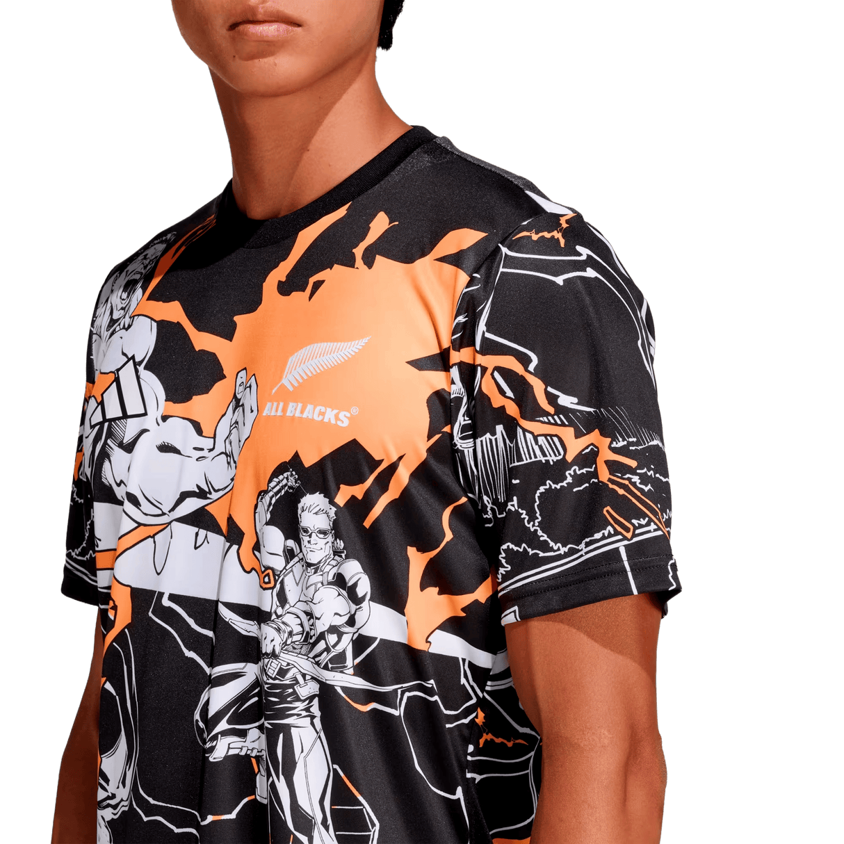 A person wears the adidas All Blacks 26/27 Captains Run Replica Jersey, featuring black and orange colors, comic-style illustrations, and the All Blacks logo on the chest.