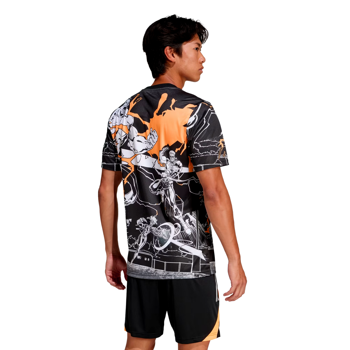 A man faces away, wearing the adidas All Blacks 26/27 Captains Run Replica Jersey with striking orange and white graphic details, paired with black shorts featuring an orange stripe.