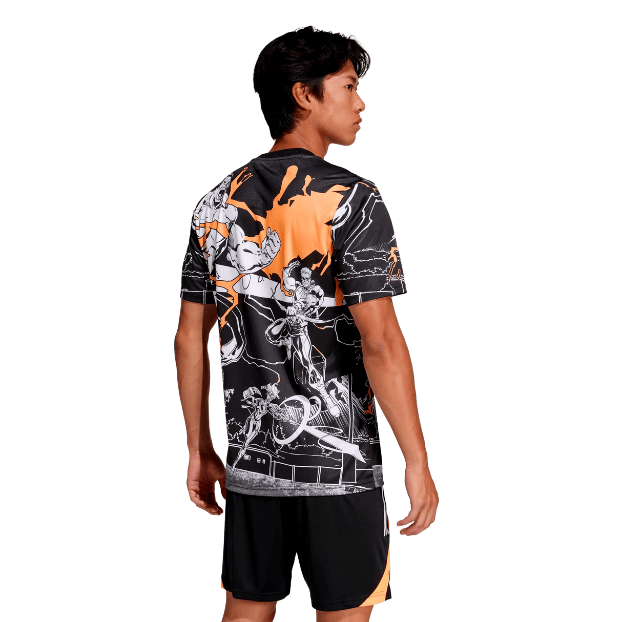A man faces away, wearing the adidas All Blacks 26/27 Captains Run Replica Jersey with striking orange and white graphic details, paired with black shorts featuring an orange stripe.