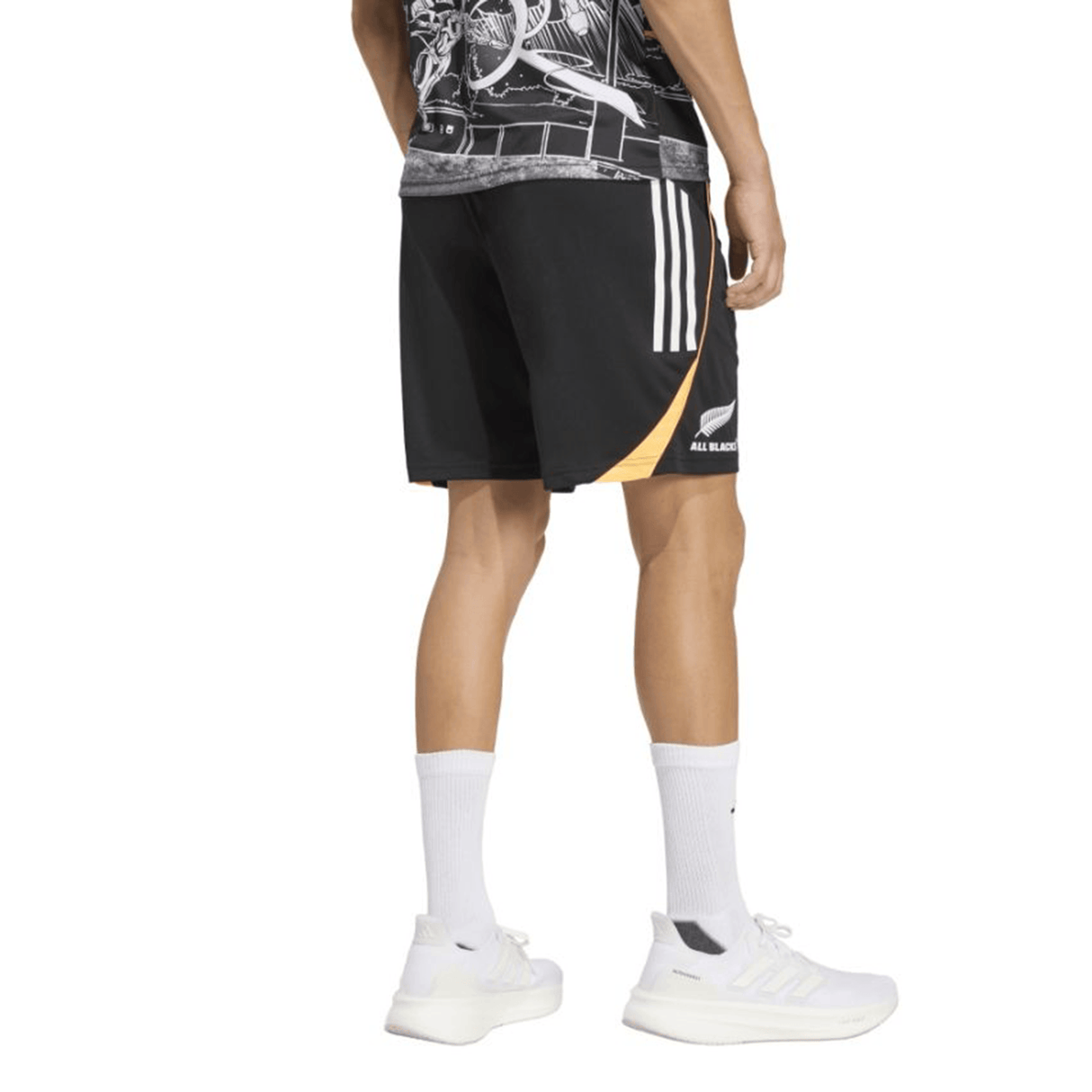 A person stands facing away, wearing adidas All Blacks 26/27 Marvel Performance Gym Shorts with white stripes, a graphic shirt, white crew socks, and white sneakers.