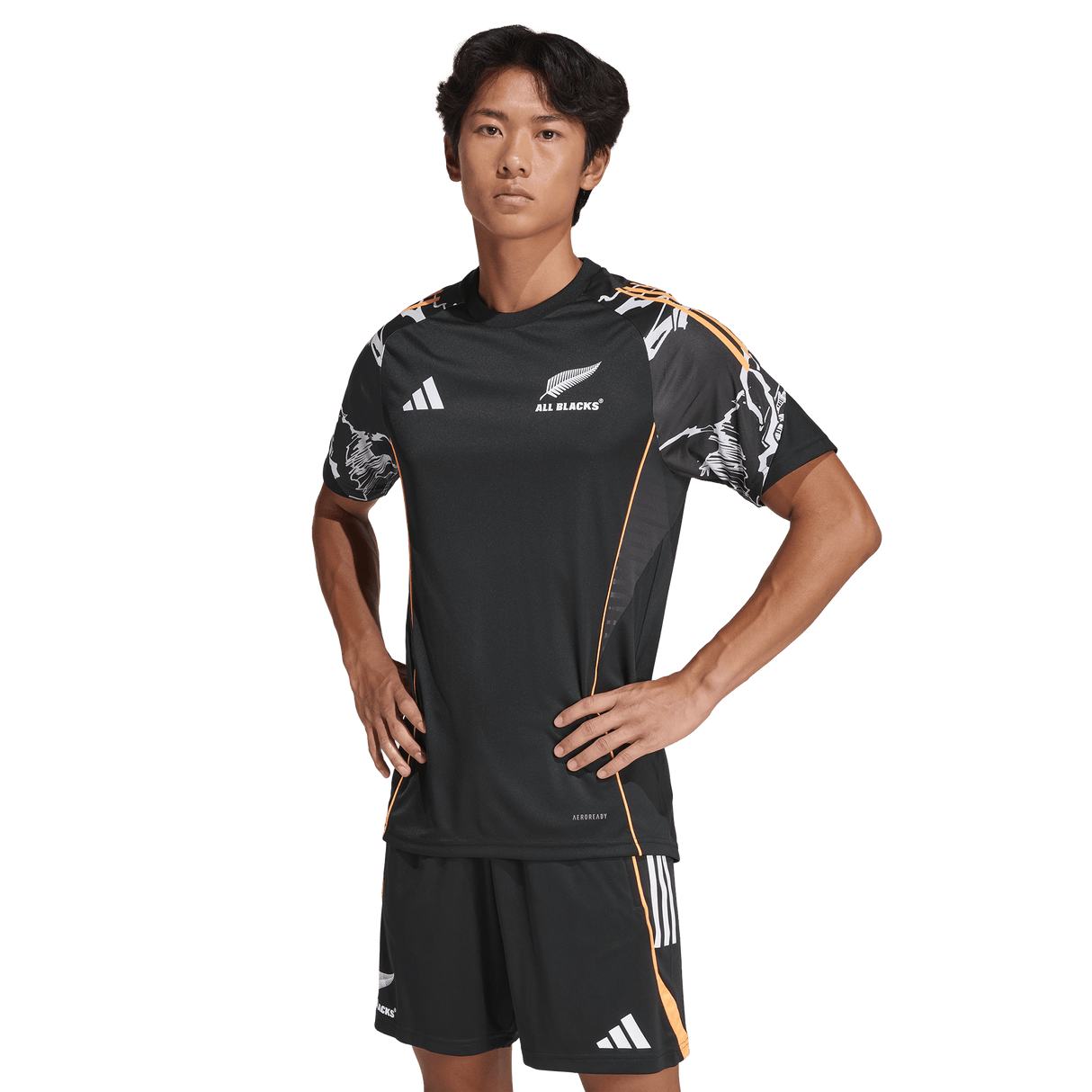 A man stands hands on hips in an adidas All Blacks 26/27 Marvel Performance Training Tee and shorts against a plain background.