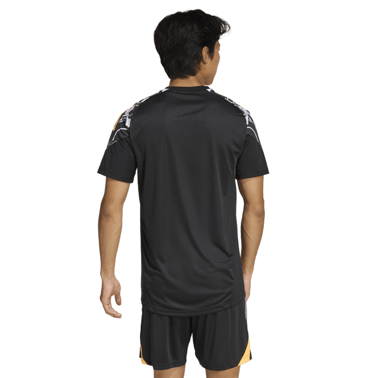 A person stands facing away, wearing the adidas All Blacks 26/27 Marvel Performance Training Tee and black shorts with yellow accents, set against a plain white background.