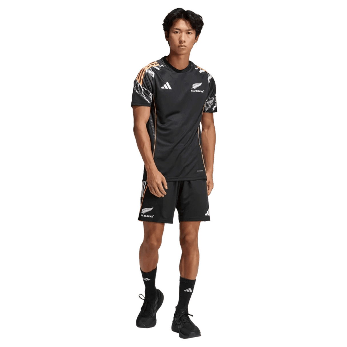 A man stands facing forward wearing a black adidas All Blacks 26/27 Marvel Performance Training Tee with logos and patterned shoulder accents, paired with matching shorts.