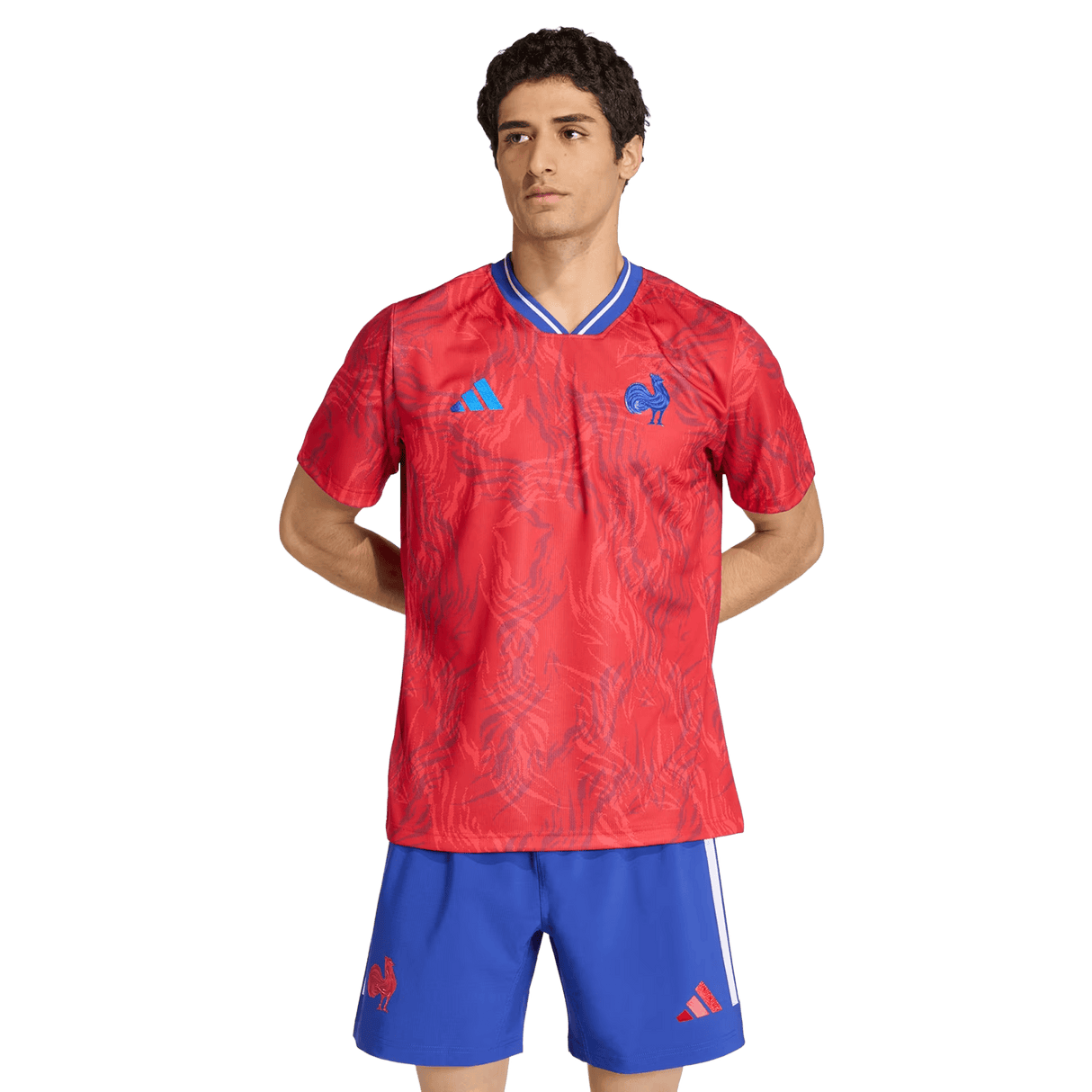 A man stands with hands behind his back, wearing the adidas France Rugby Prematch Jersey and blue shorts, both featuring logos and Climacool technology, against a plain background.
