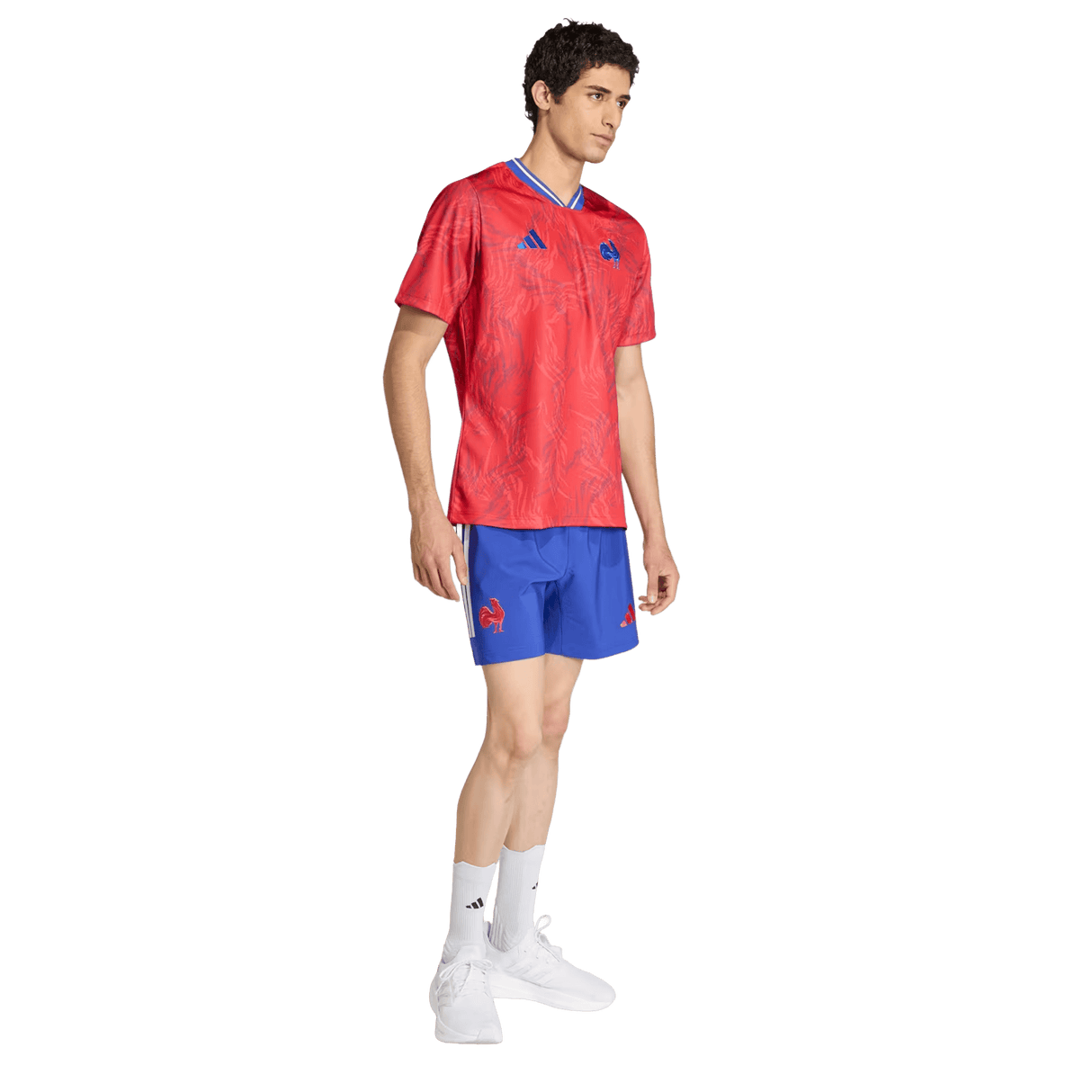 A man wears the France Rugby Prematch Jersey by adidas, blue shorts, white socks, and white athletic shoes, standing on a plain white background.