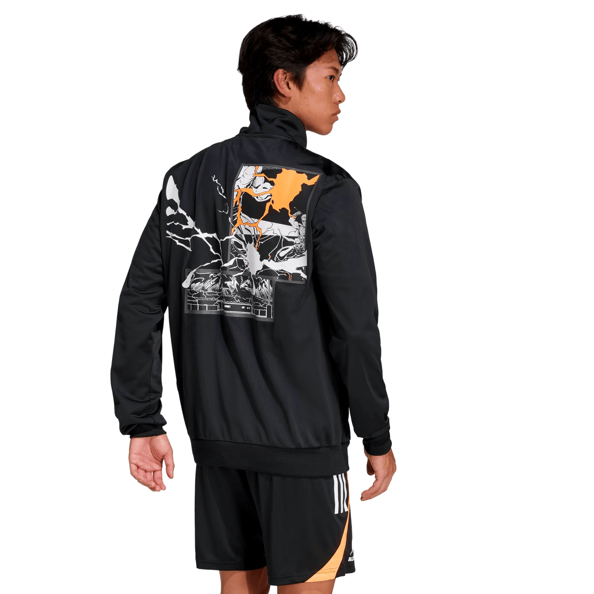 A man stands facing away in the All Blacks 26/27 Marvel Track Top by adidas, showcasing its bold graphic back design, paired with black shorts with orange and white accents for a striking Marvel-inspired sportswear look.