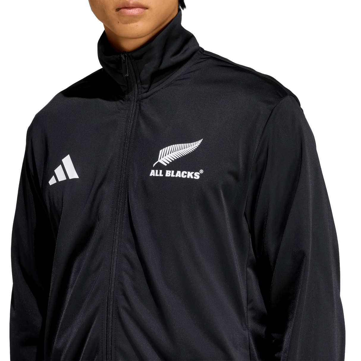 A person wearing the All Blacks 26/27 Marvel Track Top by adidas—a black zip-up jacket featuring the adidas logo and silver fern emblem, ideal rugby fan apparel.