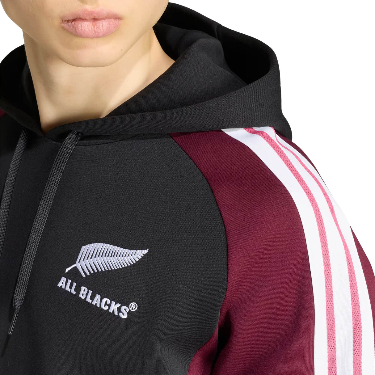 Wearing the adidas All Blacks 27/28 Hoodie in black and maroon, featuring iconic white sleeve stripes and a silver fern “ALL BLACKS” logo on the chest, this person proudly supports New Zealand rugby.