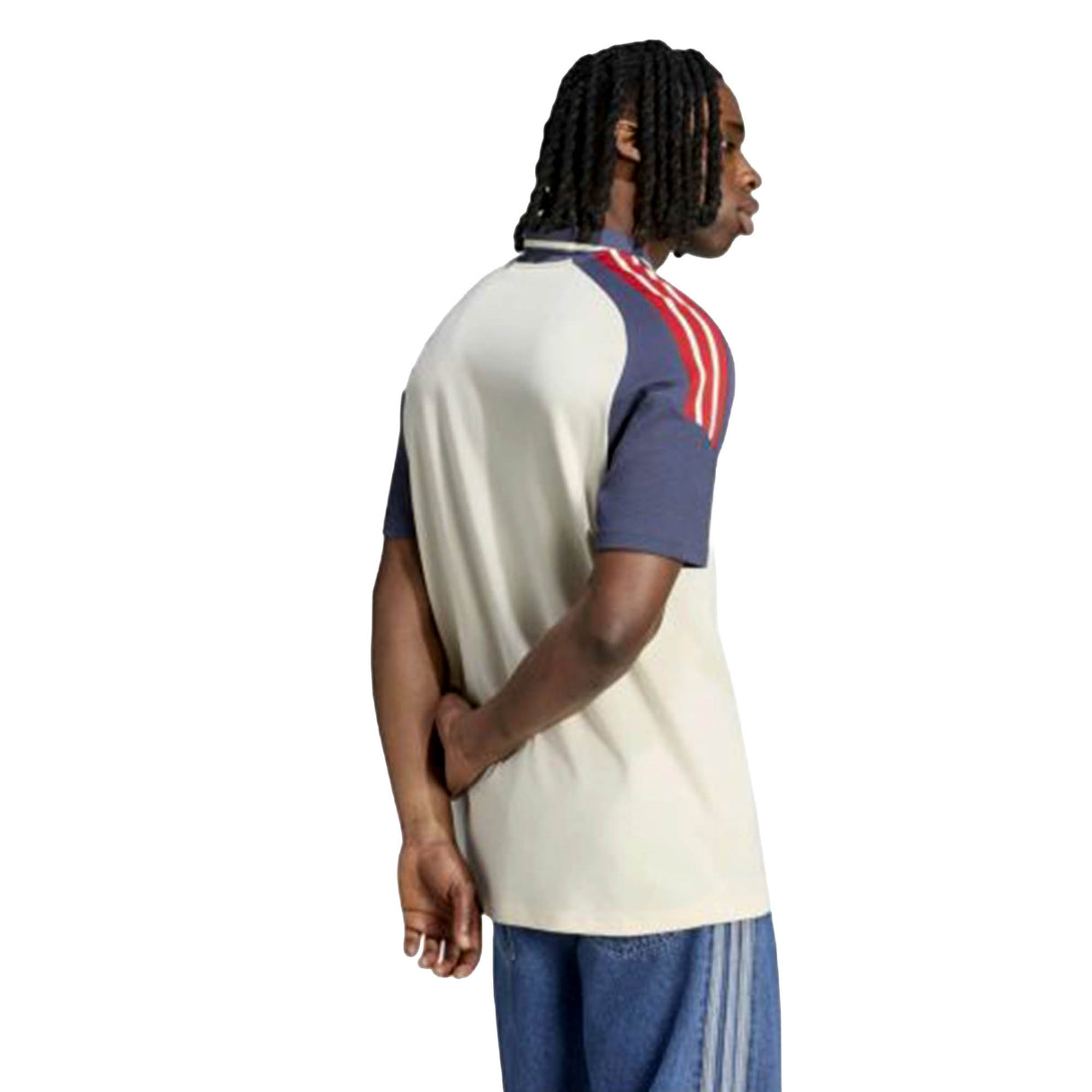 A person stands with their back to the camera, wearing the France FFR 26/27 Training Polo by adidas—a short-sleeved beige and navy rugby polo featuring red stripes on the shoulders—paired with blue jeans.