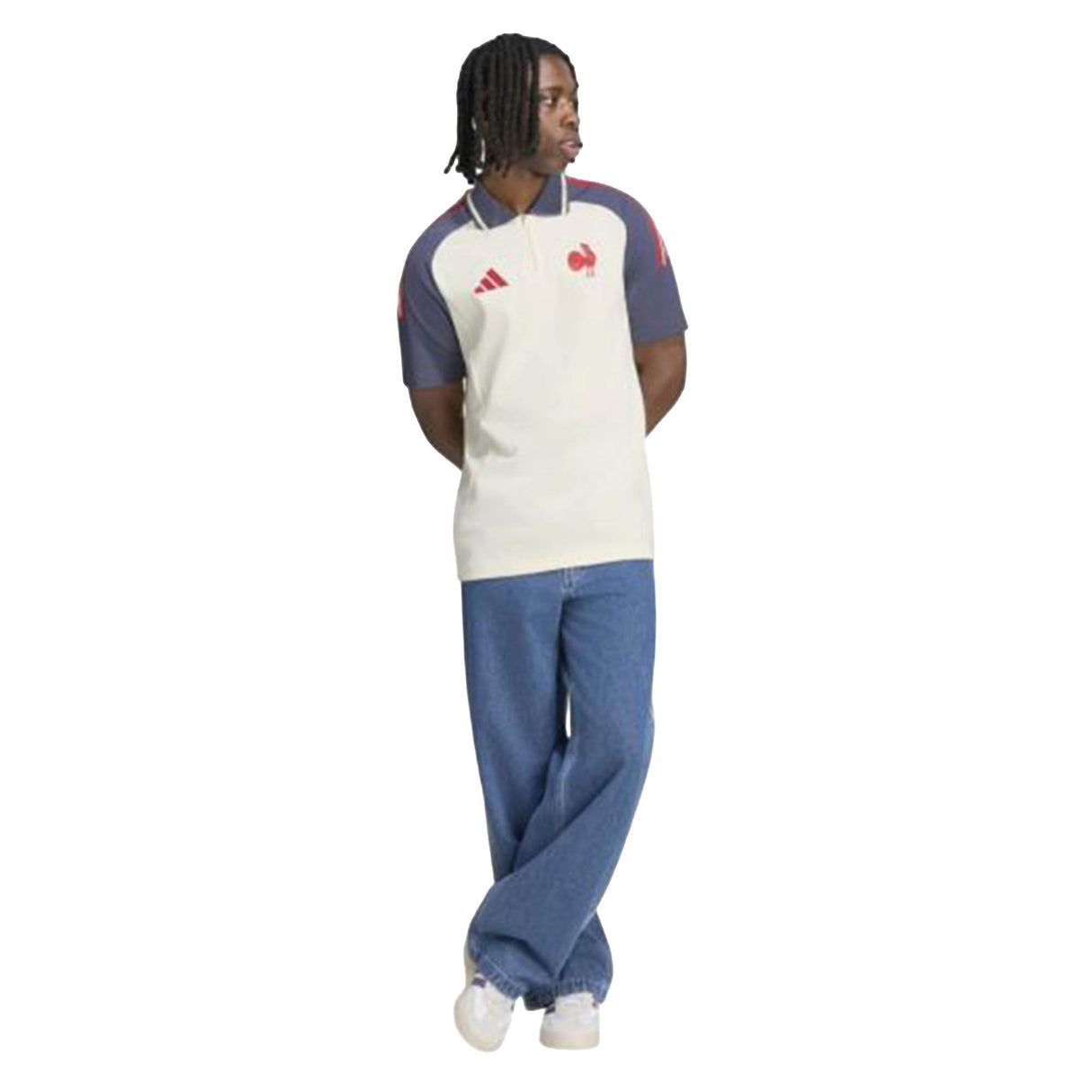 A person wearing the France FFR 26/27 Training Polo by adidas—a short-sleeve white and blue shirt with red accents—paired with blue jeans and white shoes, stands with arms behind their back against a white background.