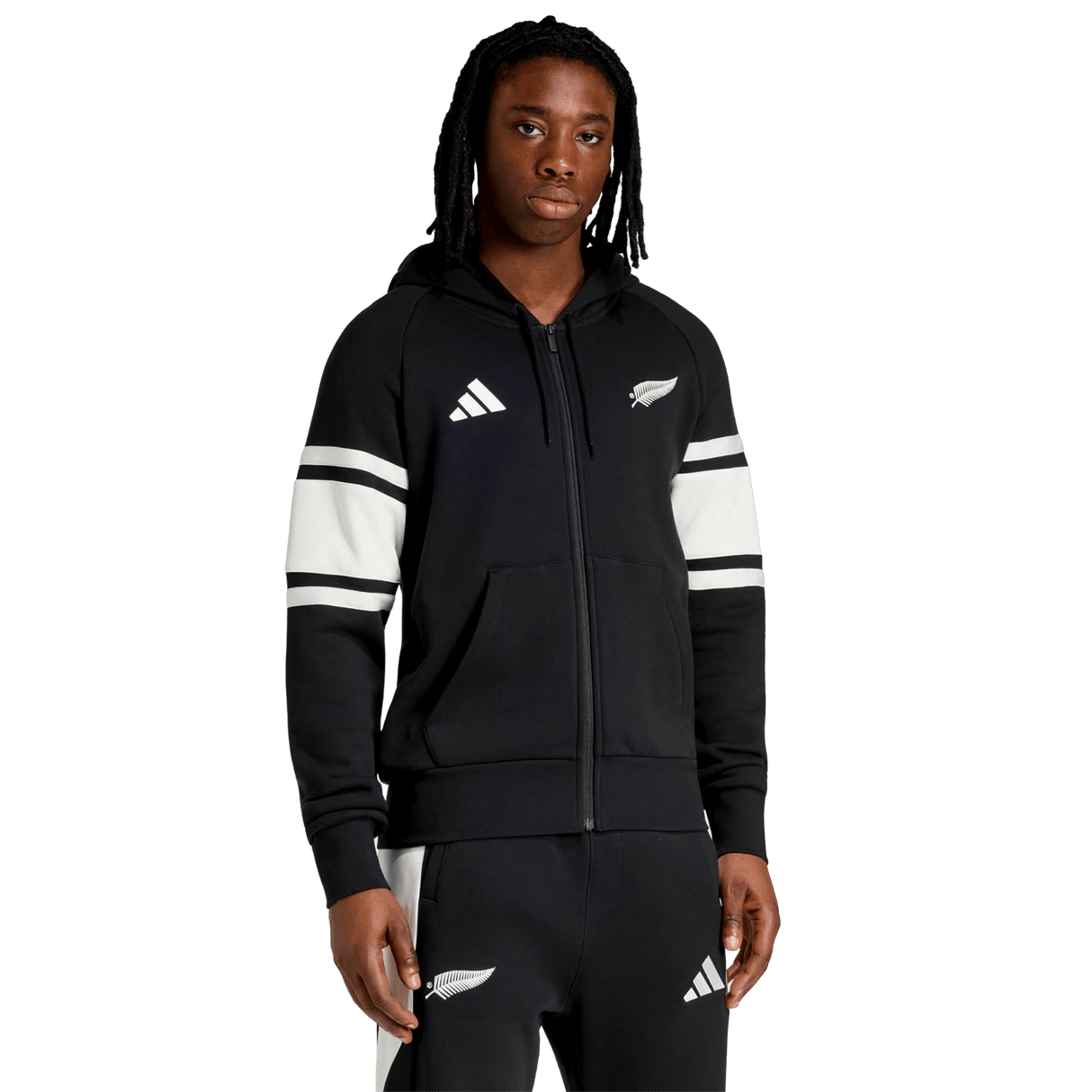 A person wears the All Blacks 26/27 Travel Full Zip Hoodie by adidas, featuring white stripes and sports logos, standing against a plain white background.