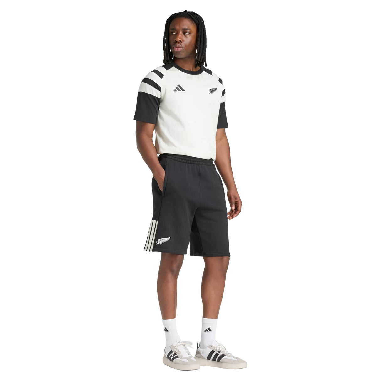 A person wearing the adidas All Blacks 26/27 Travel T-Shirt, paired with black and white adidas shorts, socks, and sneakers, stands against a white background.