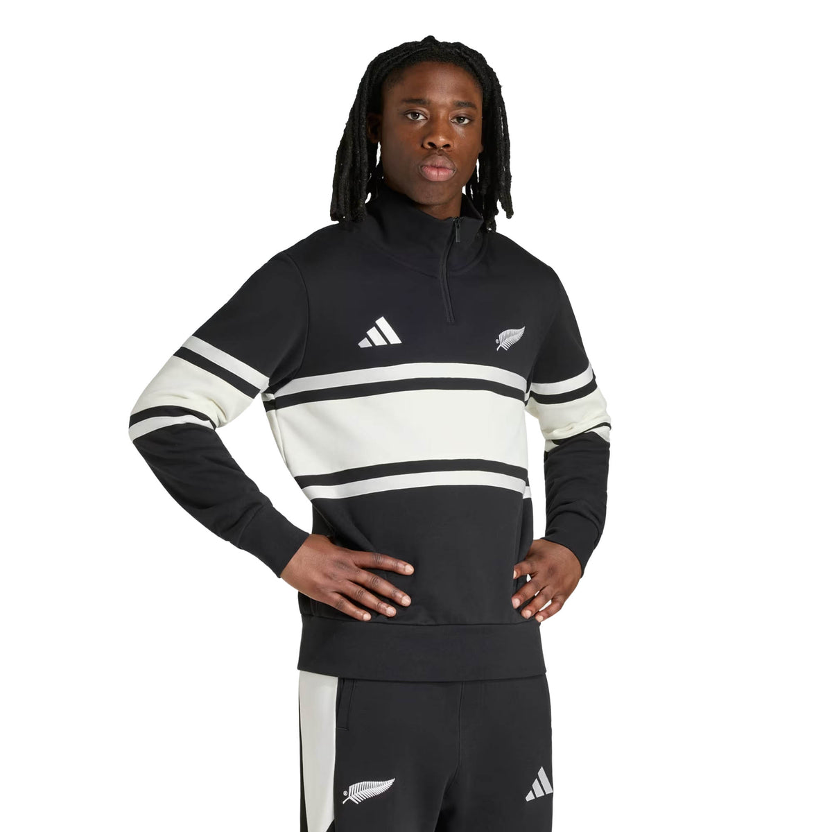 A person stands with hands on hips against a plain white background, wearing the adidas All Blacks 26/27 Leisurewear 1/4 Zip Sweatshirt in black and white.
