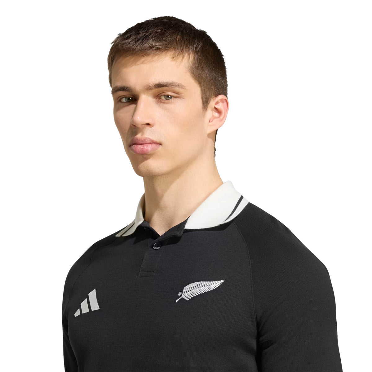 A man wearing the adidas All Blacks 26/27 Travel Polo, featuring white trim and the New Zealand Rugby insignia, stands facing slightly left against a plain background.